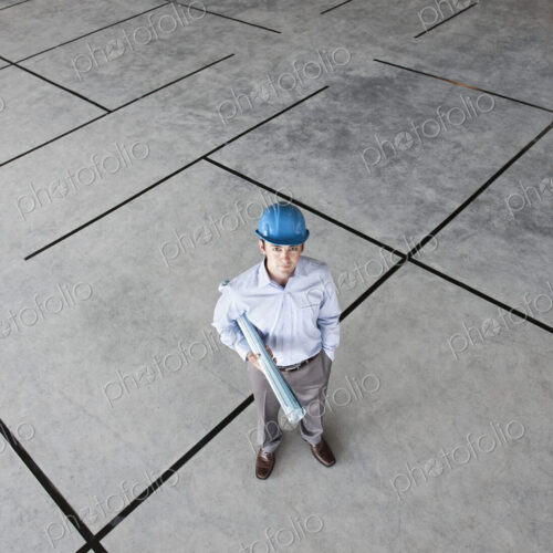 Caucasian businessman holding plans for a new office in a large empty raw office space.