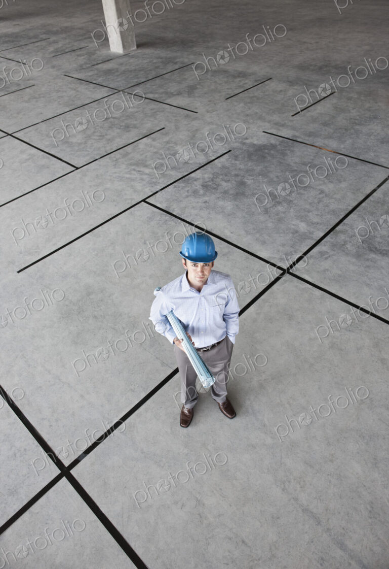 Caucasian businessman holding plans for a new office in a large empty raw office space.