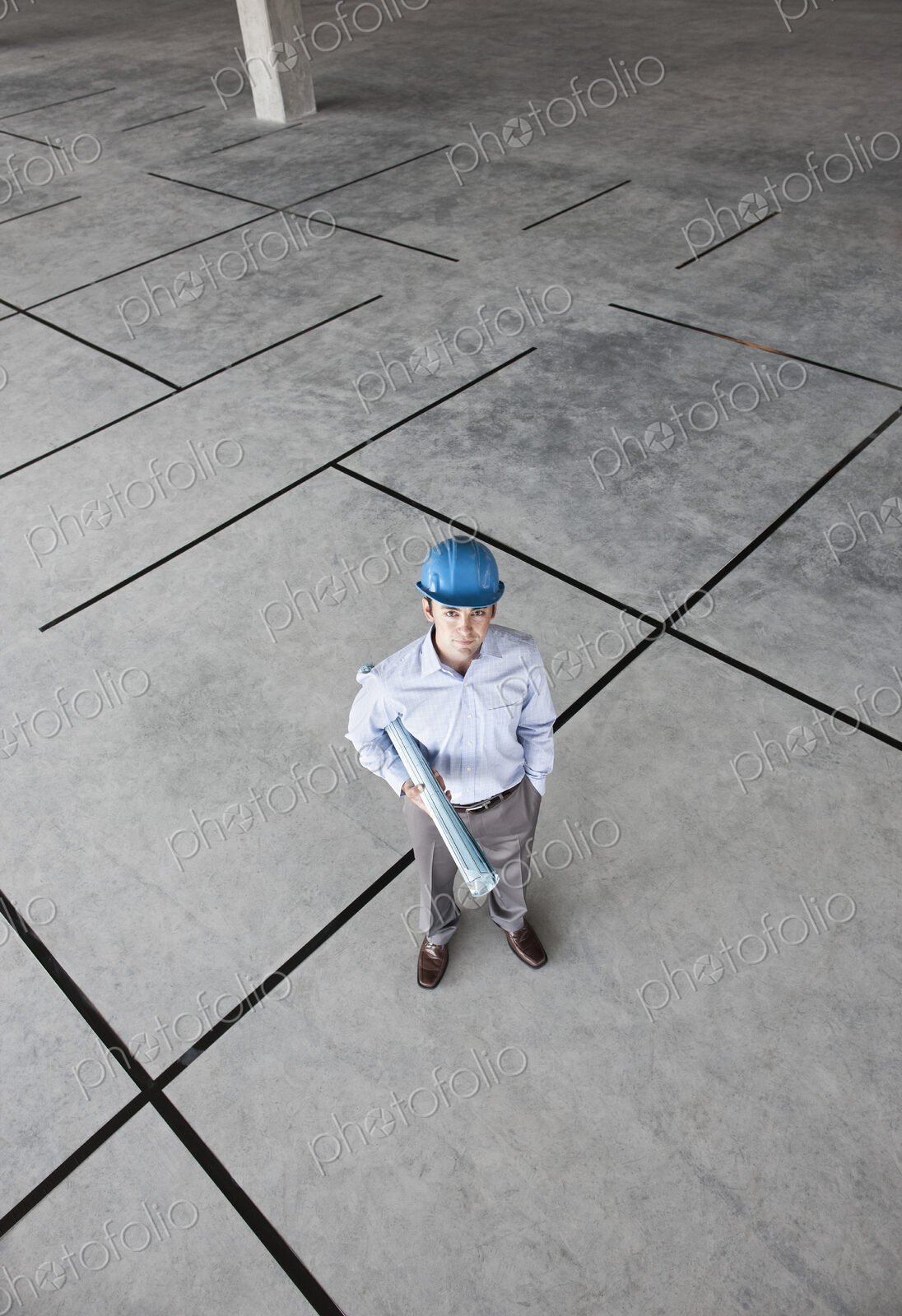 Caucasian businessman holding plans for a new office in a large empty raw office space.