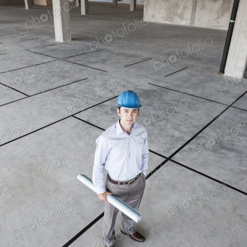 Caucasian businessman holding plans for a new office in a large empty raw office space.