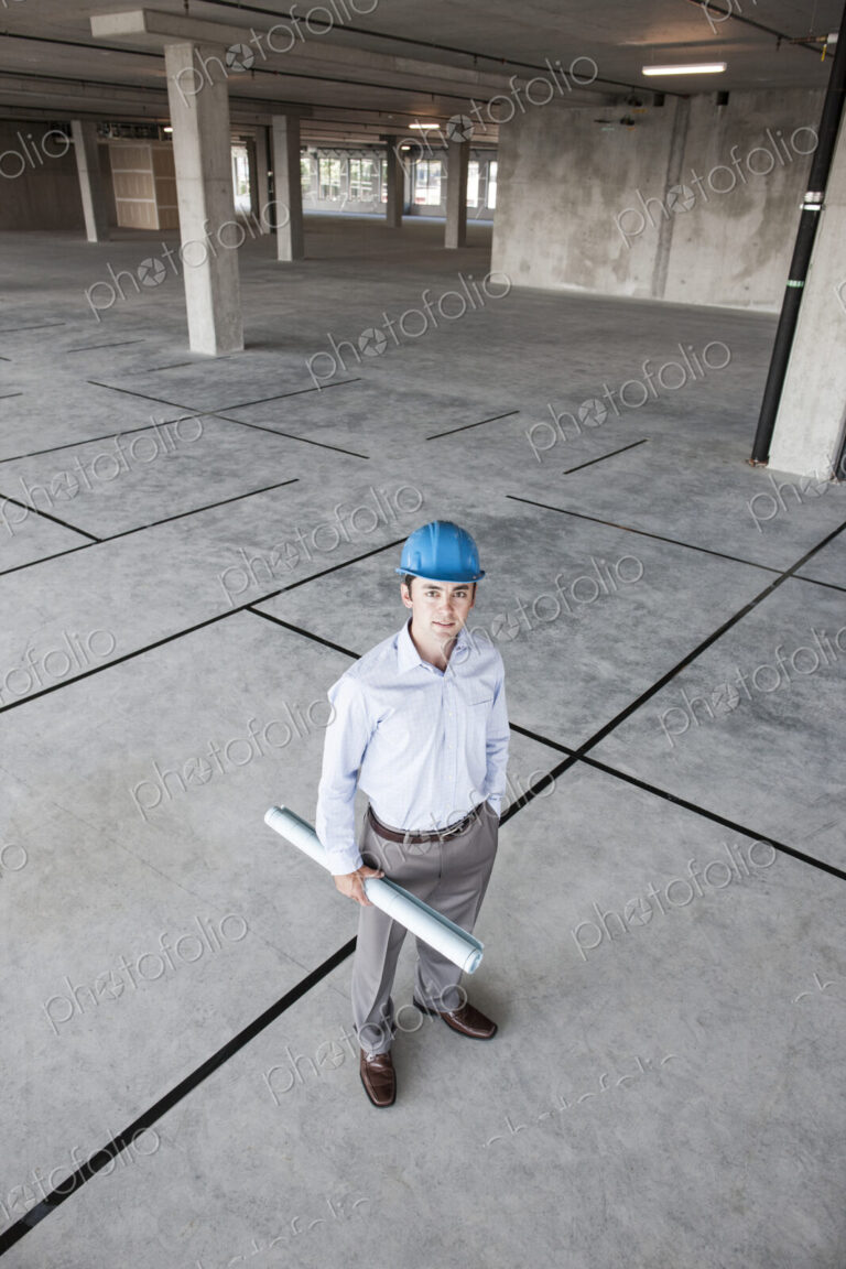 Caucasian businessman holding plans for a new office in a large empty raw office space.