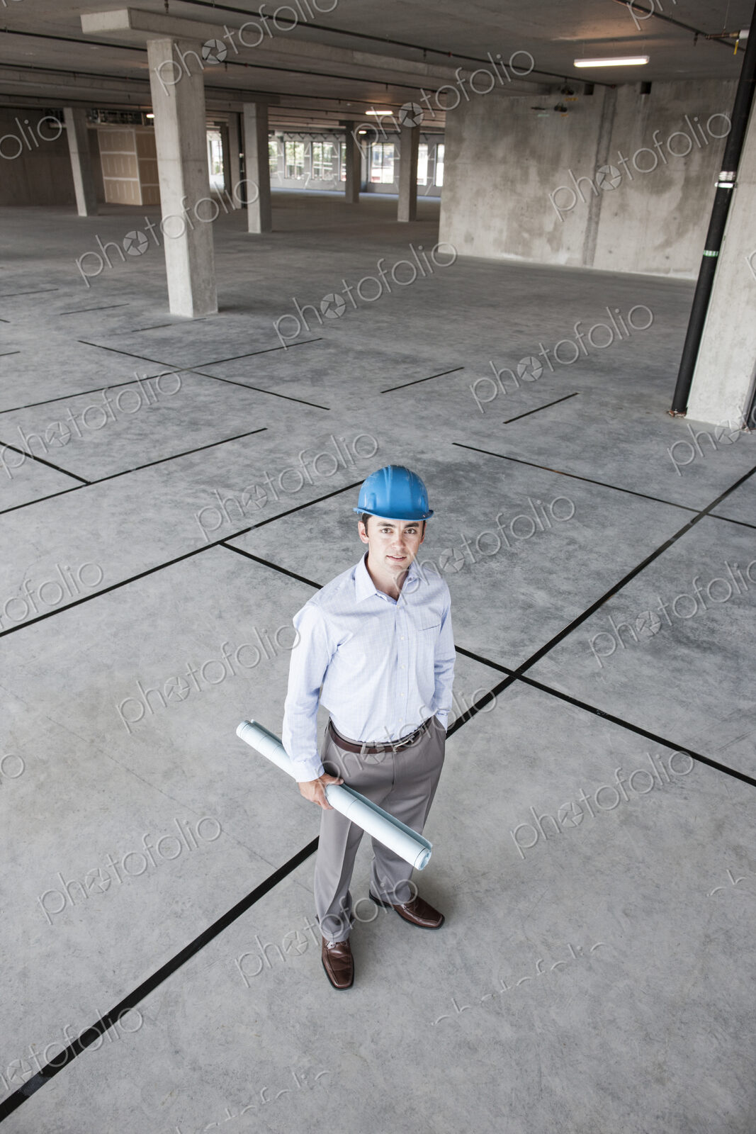Caucasian businessman holding plans for a new office in a large empty raw office space.