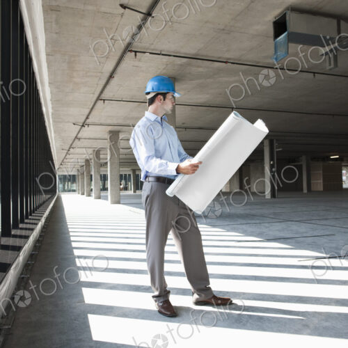 Caucasian businessman holding plans for a new office in a large empty raw office space.