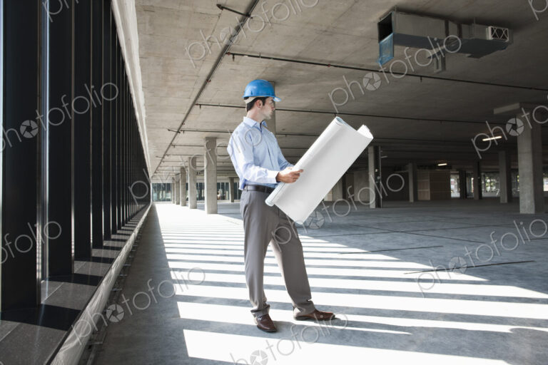 Caucasian businessman holding plans for a new office in a large empty raw office space.