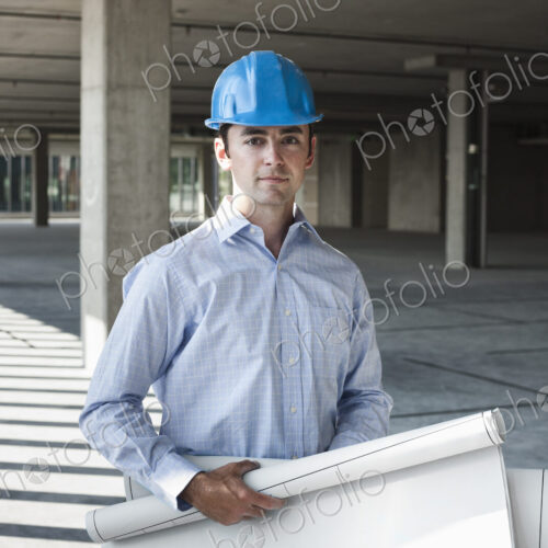 Caucasian businessman holding plans for a new office in a large empty raw office space.