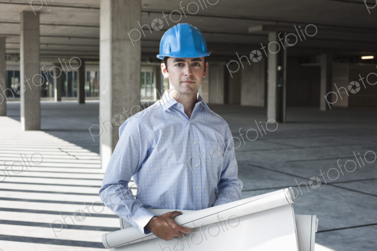Caucasian businessman holding plans for a new office in a large empty raw office space.