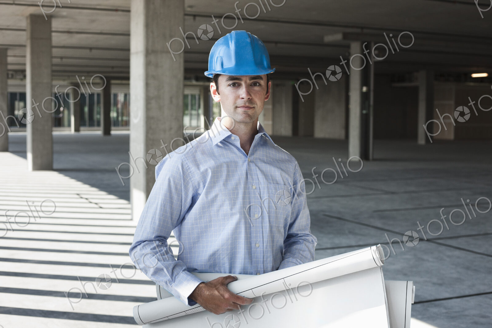 Caucasian businessman holding plans for a new office in a large empty raw office space.