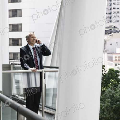 Caucasian businessman on the phone while standing on an office balcony.