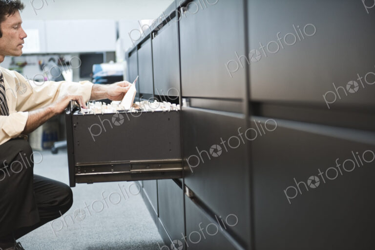 Caucasian businessman pulling files from a traditional file cabinet.