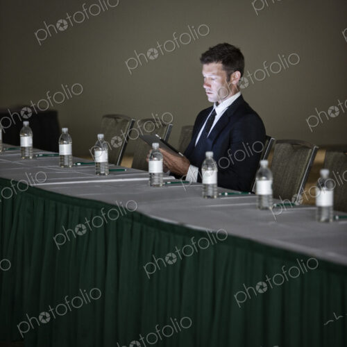 Caucasian businessman sitting alone and using a notebook computer at a convention… Caucasian businessman sitting alone and using a notebook computer at a convention…