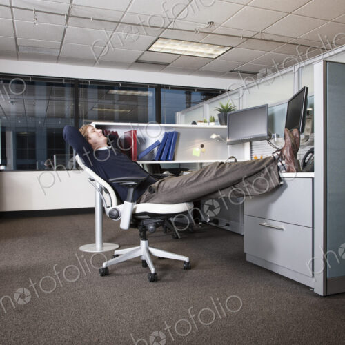 Caucasian businessman sitting in a chair with his feet on his desk in his office cubicle. Caucasian businessman sitting in a chair with his feet on his desk in his office cubicle.