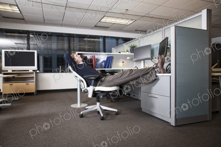 Caucasian businessman sitting in a chair with his feet on his desk in his office cubicle.