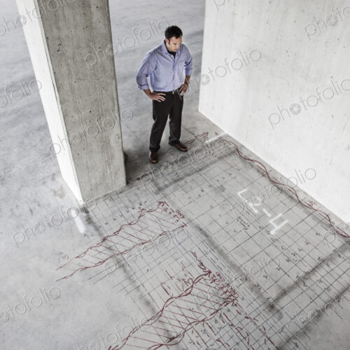 Caucasian businessman standing in a new raw office space looking at an office layout…
