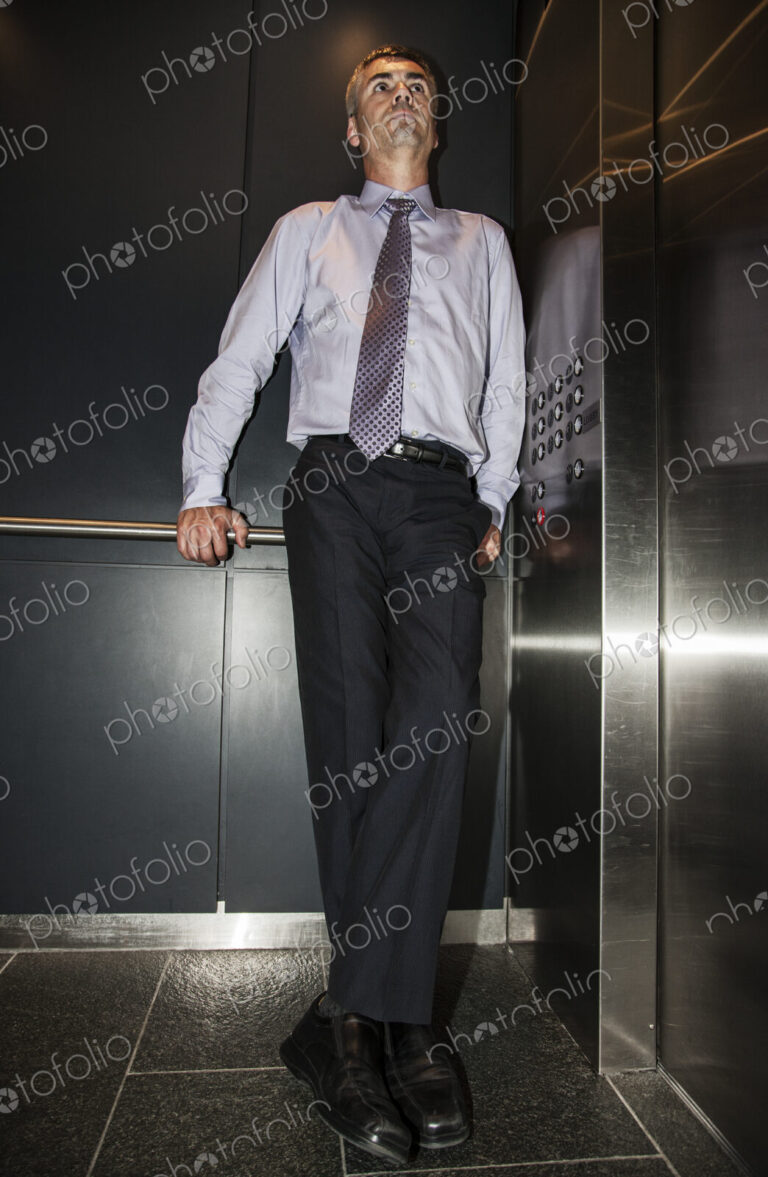 Caucasian businessman standing in the corner of an elevator in a large office building.