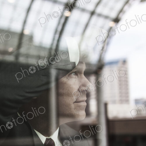 Caucasian businessman staring out a window with reflections.