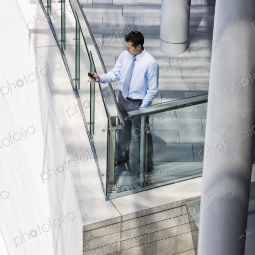 Caucasian businessman texting from a balcony on a large office building Caucasian businessman texting from a balcony on a large office building