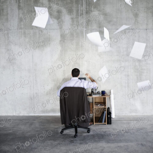 Caucasian businessman throwing papers in air while sitting at his desk in a large raw… Caucasian businessman throwing papers in air while sitting at his desk in a large raw…