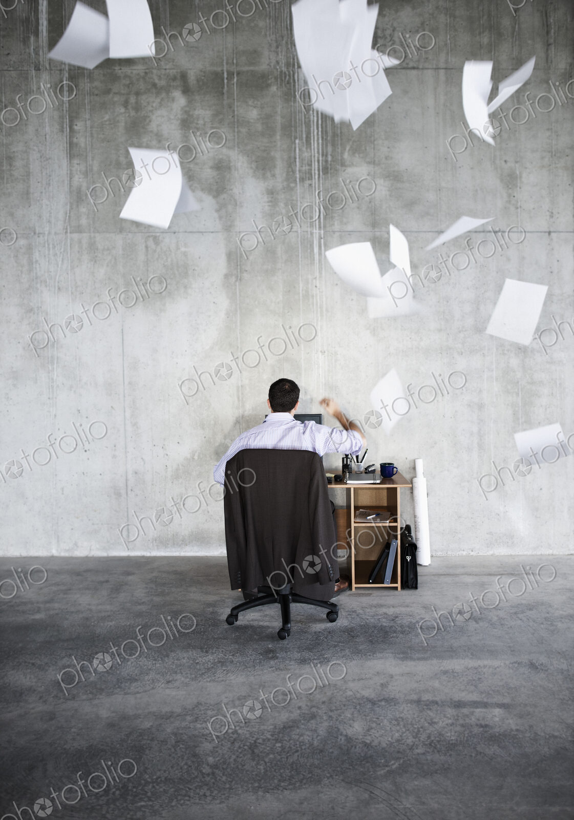 Caucasian businessman throwing papers in air while sitting at his desk in a large raw…