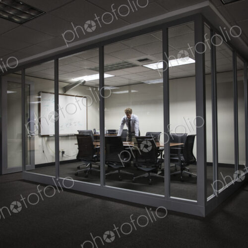 Caucasian businessman working at night in a glassed in conference room. Caucasian businessman working at night in a glassed in conference room.