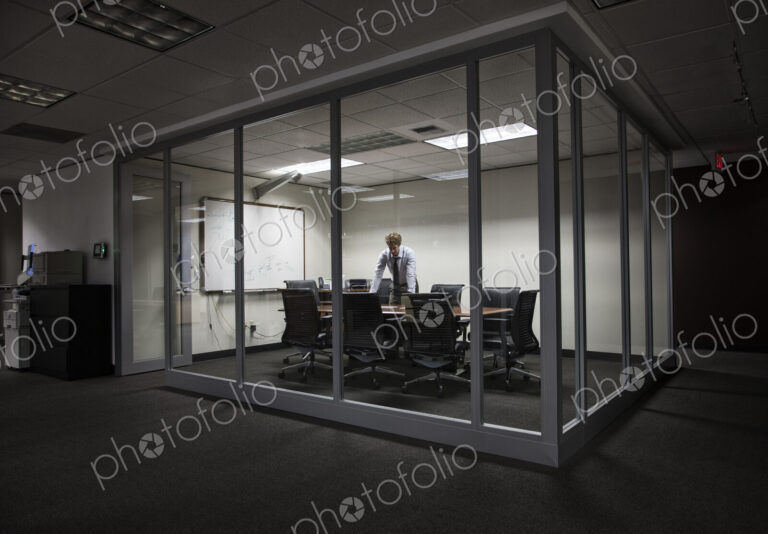 Caucasian businessman working at night in a glassed in conference room.