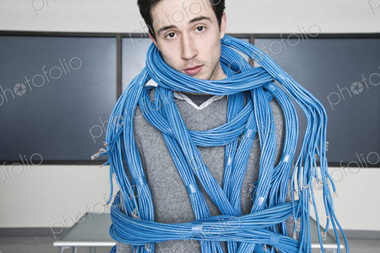 Caucasian businessman wrapped up in CAT 5 copmuter cables from a computer server farm.