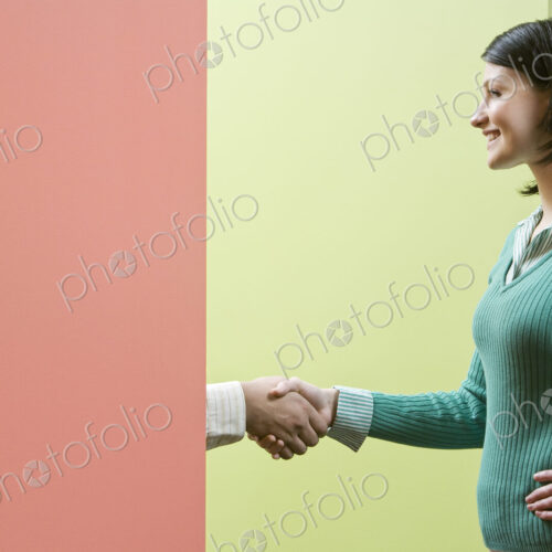 Caucasian businesswoamn shaking hands with a businessman standing behind a very…