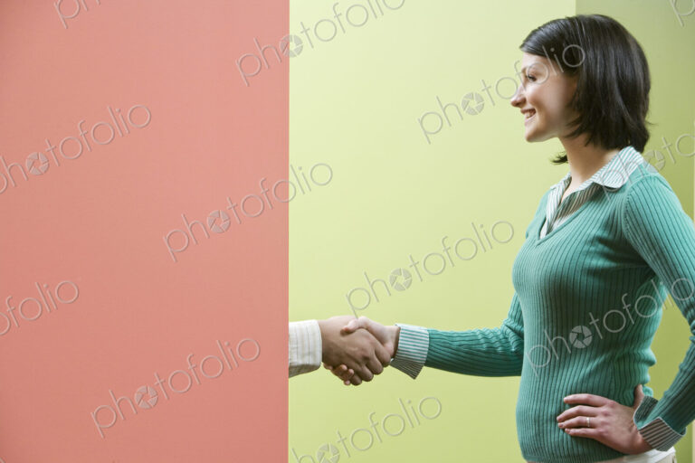 Caucasian businesswoamn shaking hands with a businessman standing behind a very…