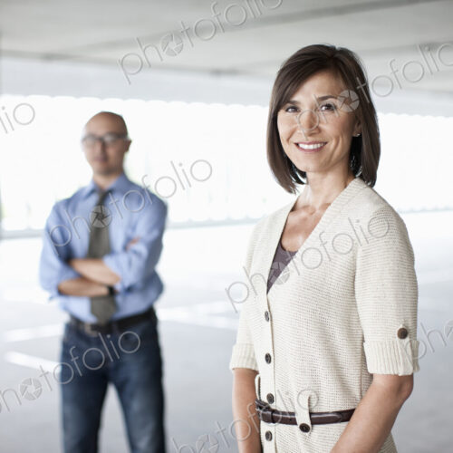 Caucasian businesswoman and Asian businessman standing in a large empty raw office space.