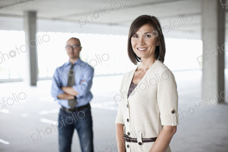 Caucasian businesswoman and Asian businessman standing in a large empty raw office space.