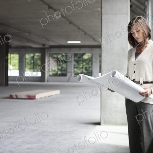 Caucasian businesswoman going over plans for a new office in a large empty raw office…