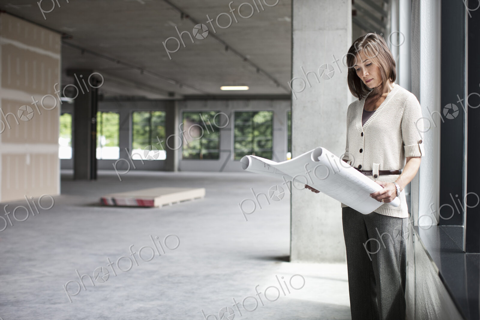 Caucasian businesswoman going over plans for a new office in a large empty raw office…