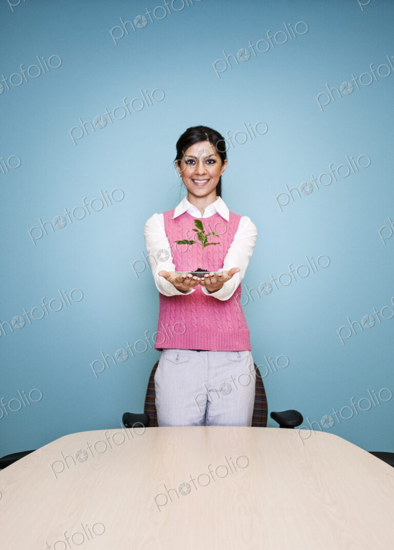 Caucasian businesswoman holding a plate with a single plant seedling.