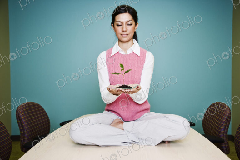 Caucasian businesswoman holding a plate with a single plant seedling.