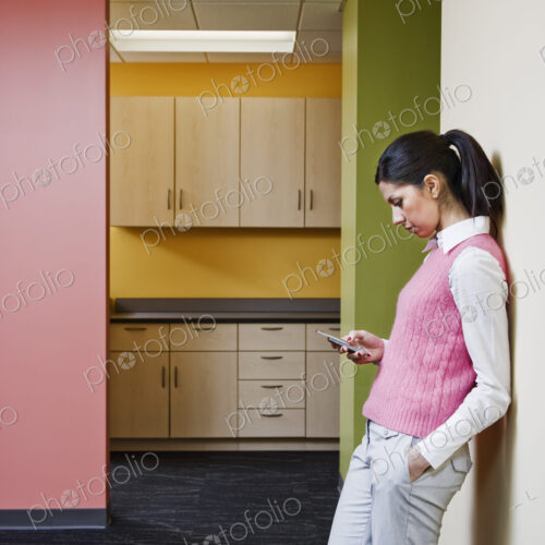 Caucasian businesswoman texting while leaning against a colorful wall in an office. Caucasian businesswoman texting while leaning against a colorful wall in an office.