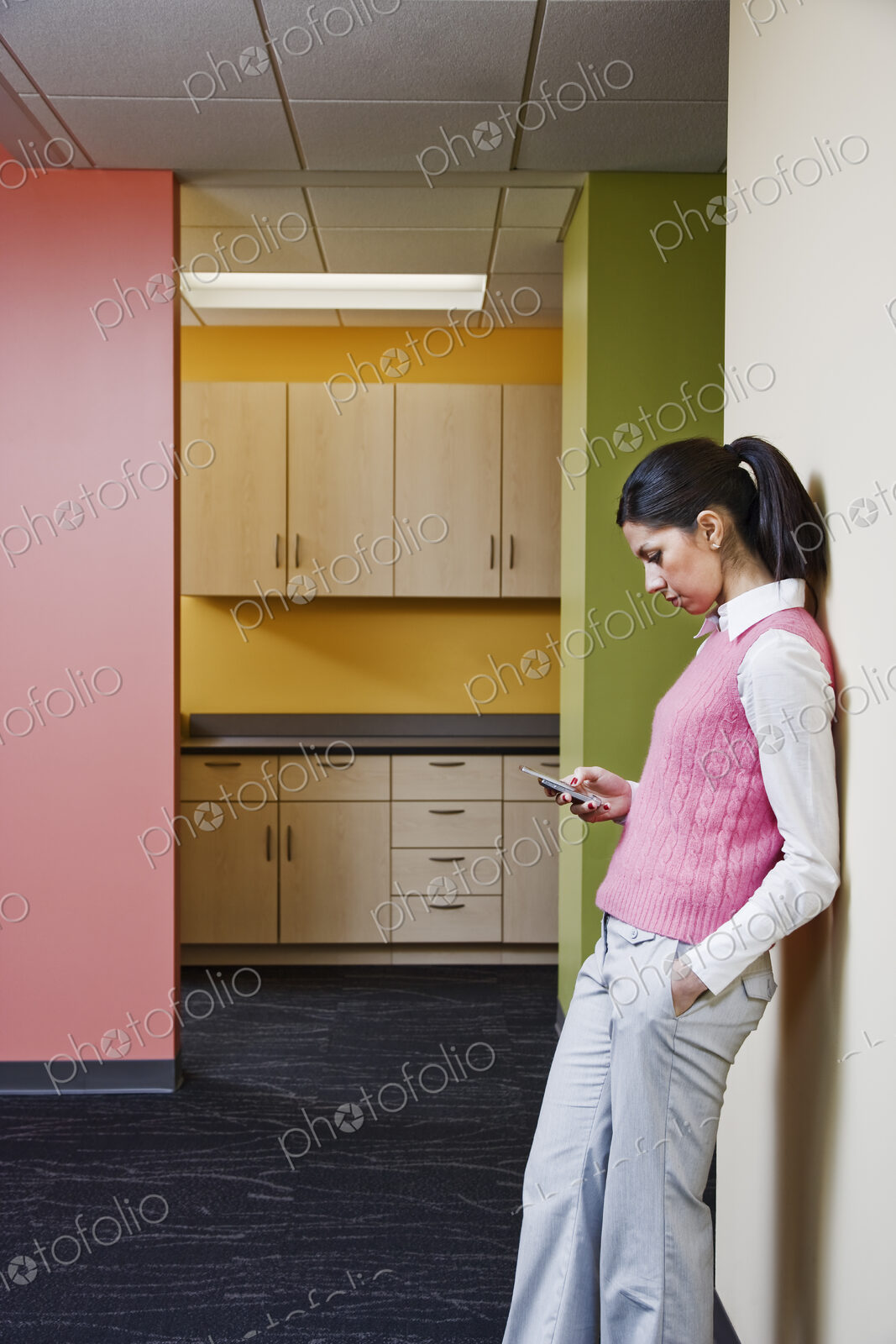 Caucasian businesswoman texting while leaning against a colorful wall in an office.