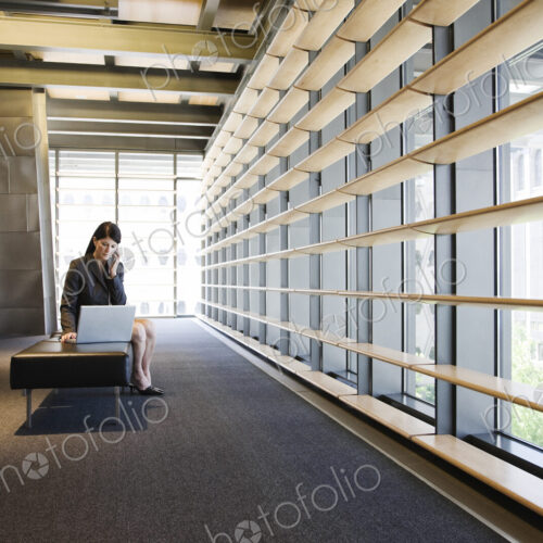 Caucasian businesswoman working on a laptop in the lobby of a large office building.