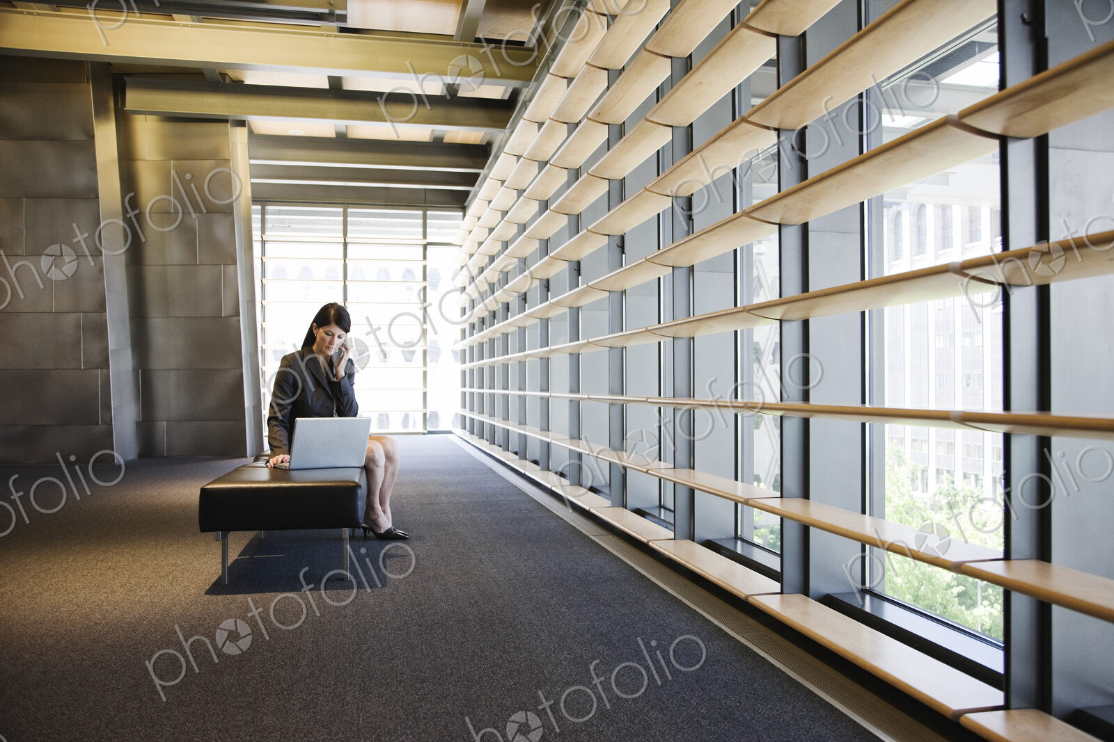 Caucasian businesswoman working on a laptop in the lobby of a large office building.