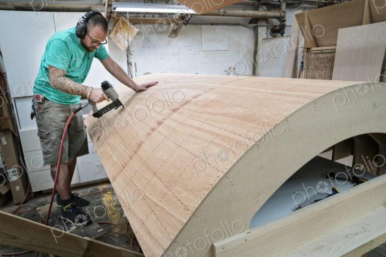 Caucasian carpenter working on a curved staircase in a large woodworking shop.