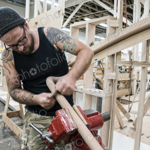 Caucasian carpenter working on a spiral staircase railing in a large woodworking shop. Caucasian carpenter working on a spiral staircase railing in a large woodworking shop.