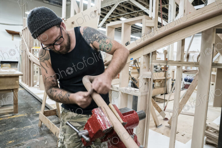 Caucasian carpenter working on a spiral staircase railing in a large woodworking shop.