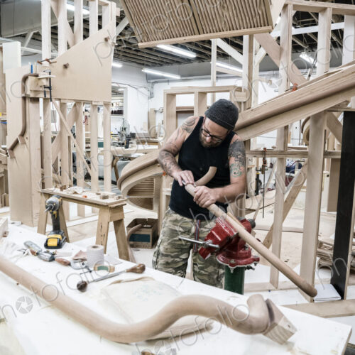 Caucasian carpenter working on a spiral staircase railing in a large woodworking shop.