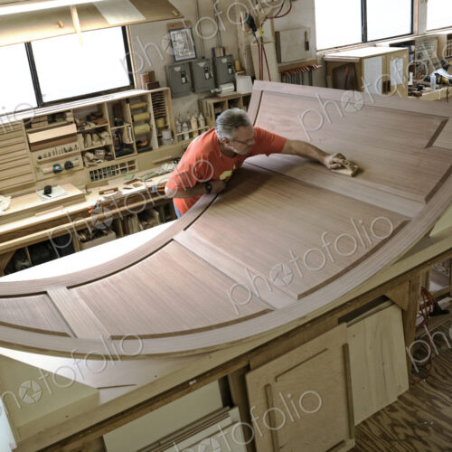 Caucasian carpenter working on curved cabinet face in a large woodworking shop.