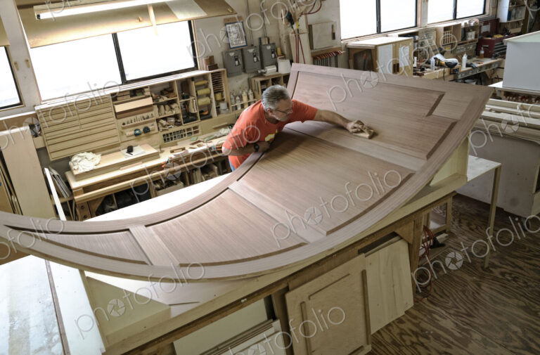 Caucasian carpenter working on curved cabinet face in a large woodworking shop.