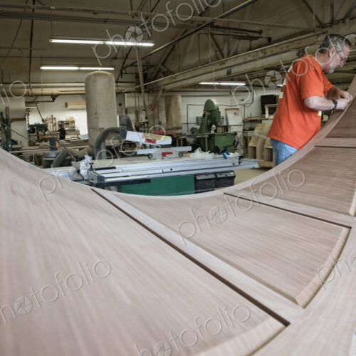 Caucasian carpenter working on curved cabinet face in a large woodworking shop.
