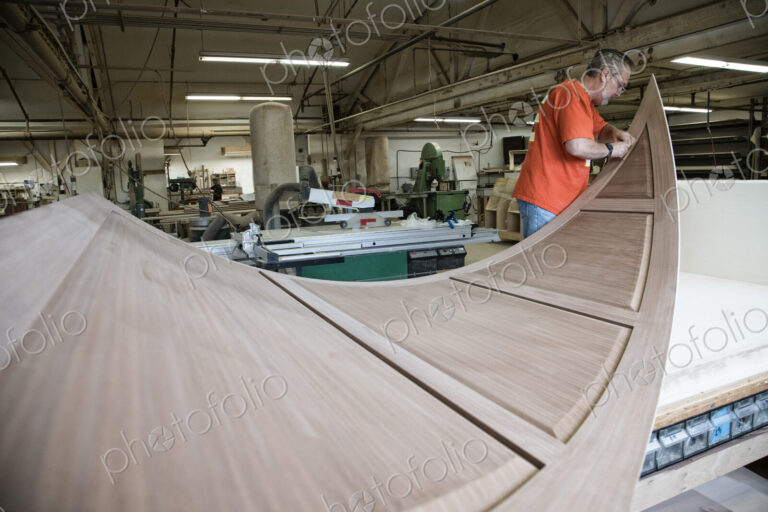 Caucasian carpenter working on curved cabinet face in a large woodworking shop.