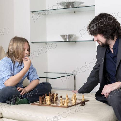 Caucasian father and son playing chess on sofa Caucasian father and son playing chess on sofa