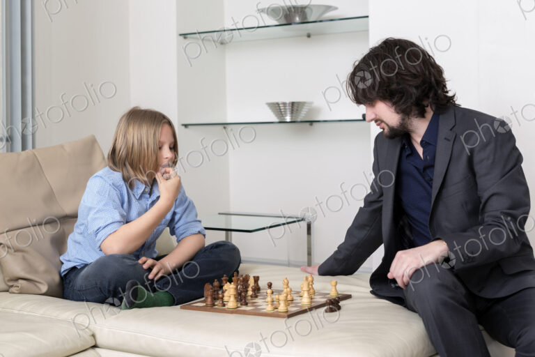 Caucasian father and son playing chess on sofa