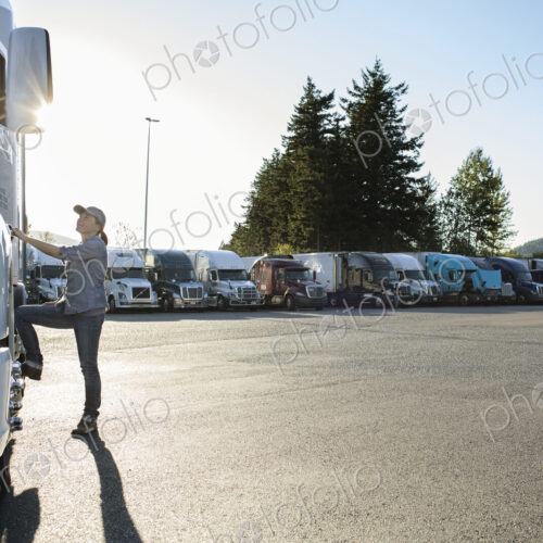 Caucasian female truck driver getting into her truck parked in a lot at a truck stop. Caucasian female truck driver getting into her truck parked in a lot at a truck stop.