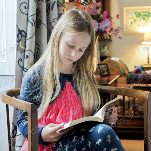 Caucasian girl reading book in armchair