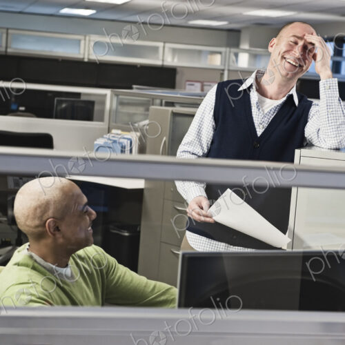 Caucasian male and black male talking and smiling in a cubicle office setting. Caucasian male and black male talking and smiling in a cubicle office setting.